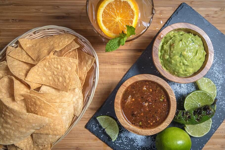 Tortilla chips in a basket beside bowls of guacamole and salsa with fresh limes